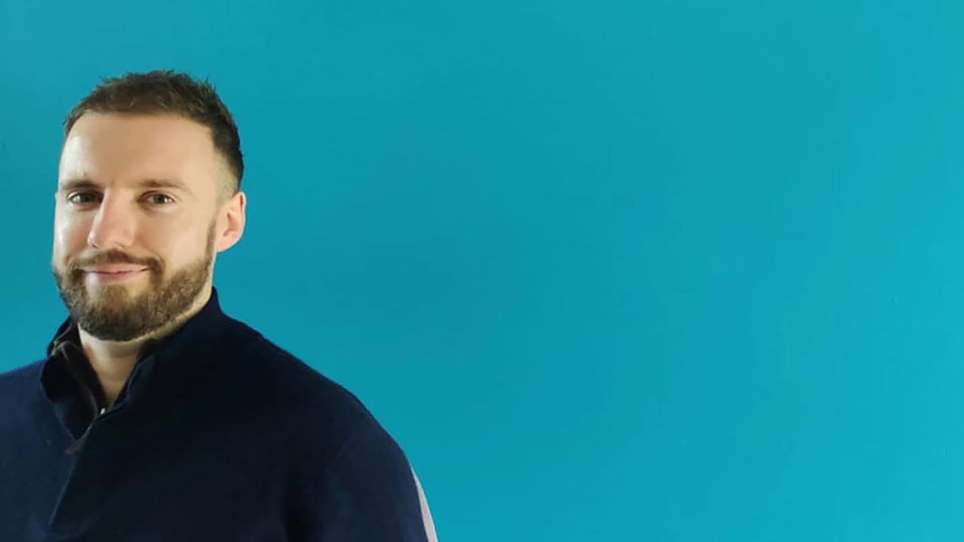 Headshot of Aaron stood against a blue background.