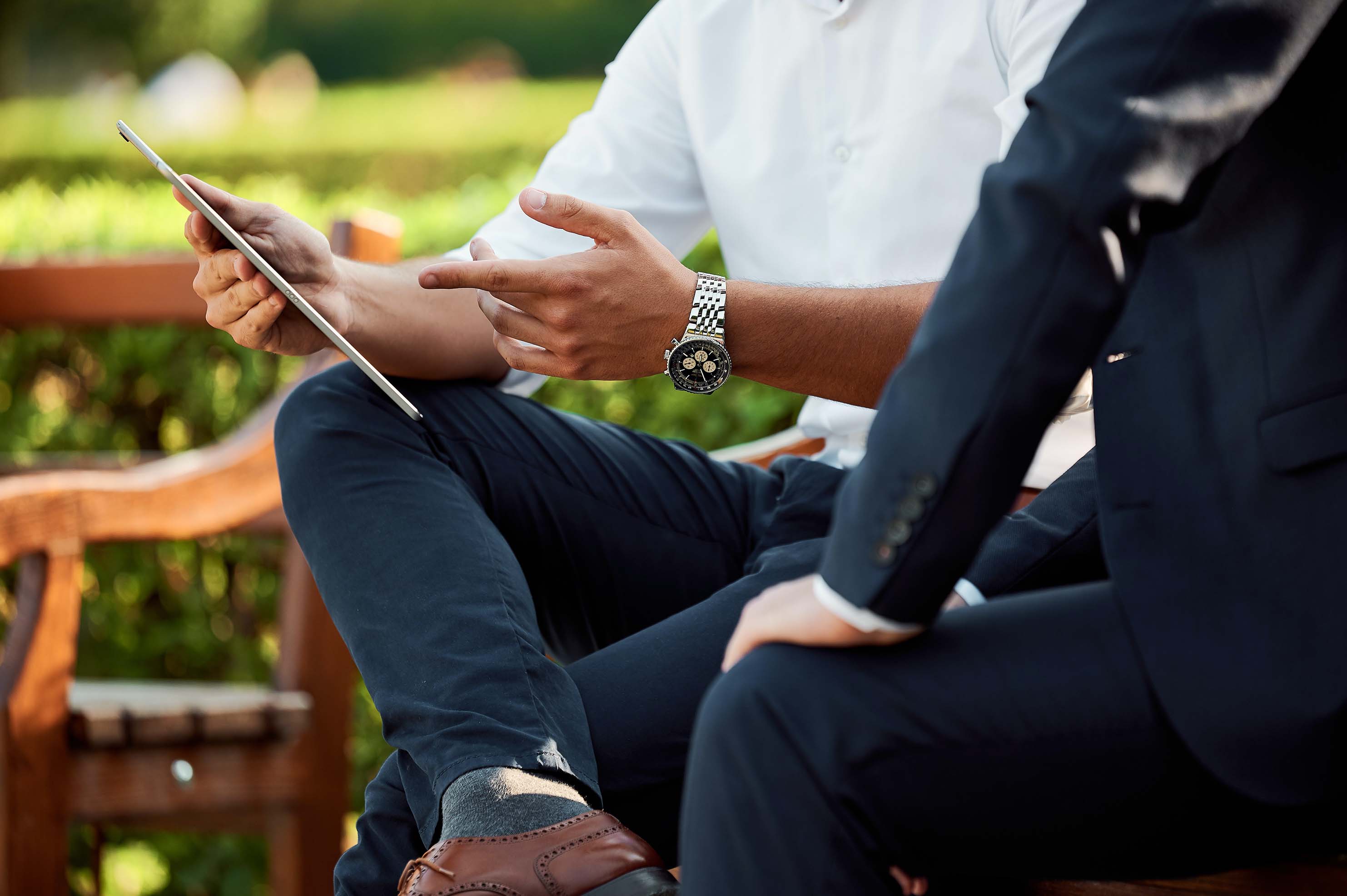 Two people sitting outside on a bench, a man in a white shirt is explaining something to a woman